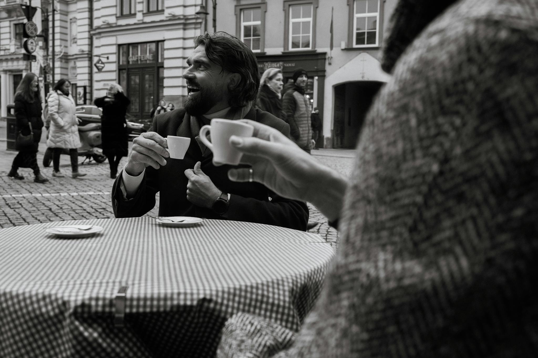 Two people enjoying coffee in an outdoor Vilnius street cafe scene, black and white.